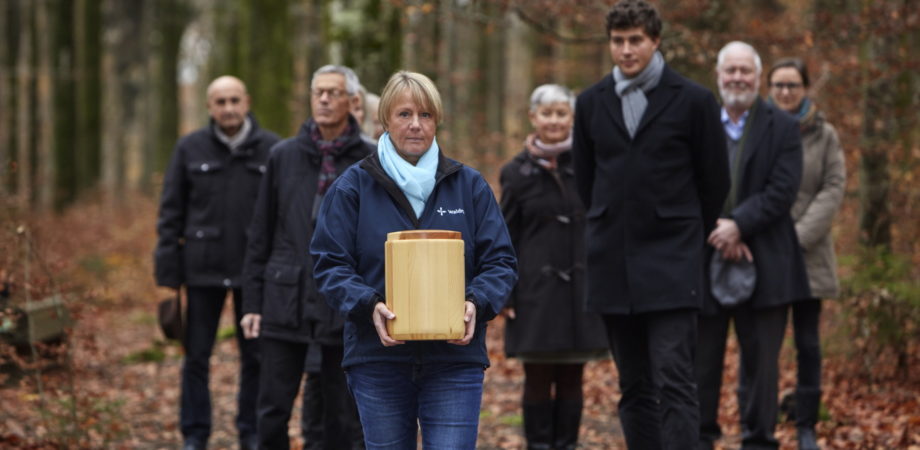 Trauergesellschaft auf dem Gang zur Grabstelle. Eine Mitarbeiterin der Waldruh trägt die Urne.